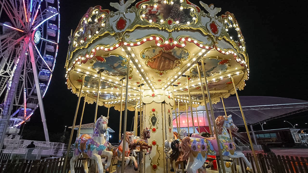 Carrossel iluminado com cavalos decorativos e roda gigante ao fundo