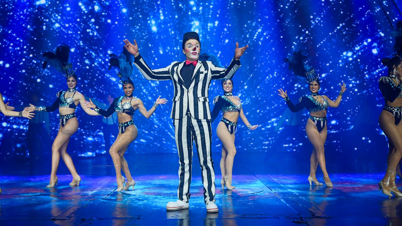 Palhaço e dançarinas em performance com fundo estrelado azul